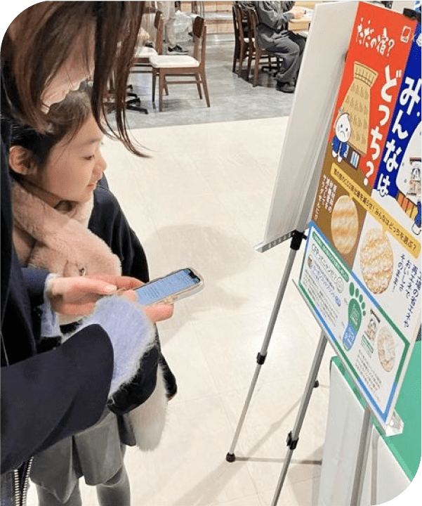 カーボンフットプリントについて書かれた看板を見る親子